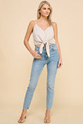 Load image into Gallery viewer, Model wearing the Dove Front Tie Cropped Tank Top in Natural, featuring a V-neckline and front tie detail, paired with high-waisted jeans and sandals for a chic, coordinated outfit.