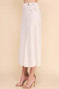 Load image into Gallery viewer, Side view of the Dove Linen Wrap Midi Skirt in Natural, showcasing the wrap silhouette, side tie detail, and effortless drape.