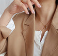 Load image into Gallery viewer, Model wearing the Anya Infinity Pendant Necklace in Gold, with a white top and tan collared jacket, for a classic and elegant look.