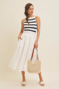 Load image into Gallery viewer, Model pairing the navy and white striped boat neck tank top with a white flowy midi skirt and a crochet tote bag, creating an effortless, chic spring outfit.
