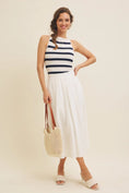 Load image into Gallery viewer, Model pairing the navy and white striped boat neck tank top with a white flowy midi skirt and a crochet tote bag, creating an effortless, chic spring outfit.
