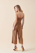 Load image into Gallery viewer, Back view of model wearing the Shiloh Smocked Tube Top Jumpsuit in Camel paired with block-heel sandals to complete this chic, warm-weather outfit.