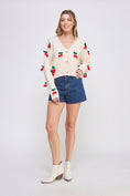 Load image into Gallery viewer, Woman wearing a cream cardigan with red cherry patterns, denim shorts, and white boots on a light gray background
